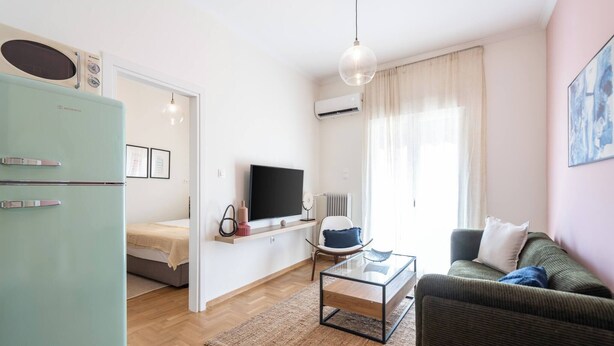 A modern living room with a television, sofa, coffee table, and a light blue refrigerator.