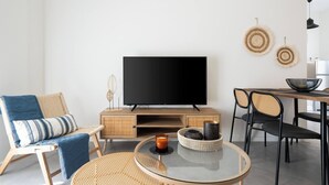 A modern living room with a flat-screen TV, wicker furniture, and a glass coffee table. - 1BR Spacious Apt | Near Metro | Beautiful View (Athens)