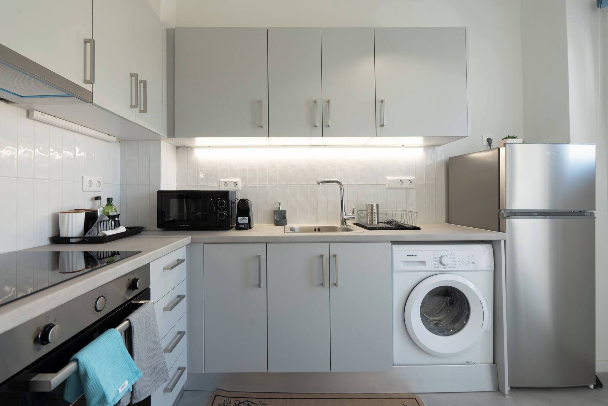 Een moderne keuken met witte kasten, een ingebouwde wasmachine, een koelkast en een magnetron.