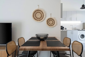 A modern kitchen with white cabinets, a washing machine, and a dining area with a wooden table and four chairs.