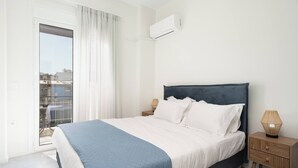 A bedroom with a bed, a nightstand, a lamp, and a view of the outside. - 1BR Spacious Apt | Near Metro | Beautiful View (Athens)