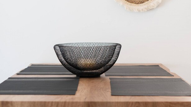 A dining table with a woven basket centerpiece, two woven wall hangings, and black chairs. - 1BR Spacious Apt | Near Metro | Beautiful View (Athens)
