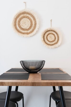 A dining table with a woven basket centerpiece, two woven wall hangings, and black chairs. - 1BR Spacious Apt | Near Metro | Beautiful View (Athens)