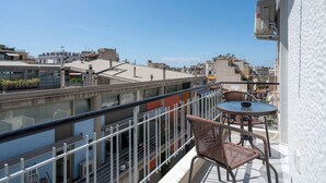A balcony with wicker chairs and a small table, overlooking a cityscape with various buildings. - 1BR Spacious Apt | Near Metro | Beautiful View (Athens)