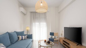 A modern living room with a sofa, TV, and a glass coffee table. - 1BR Spacious Apt | Near Metro | Beautiful View (Athens)