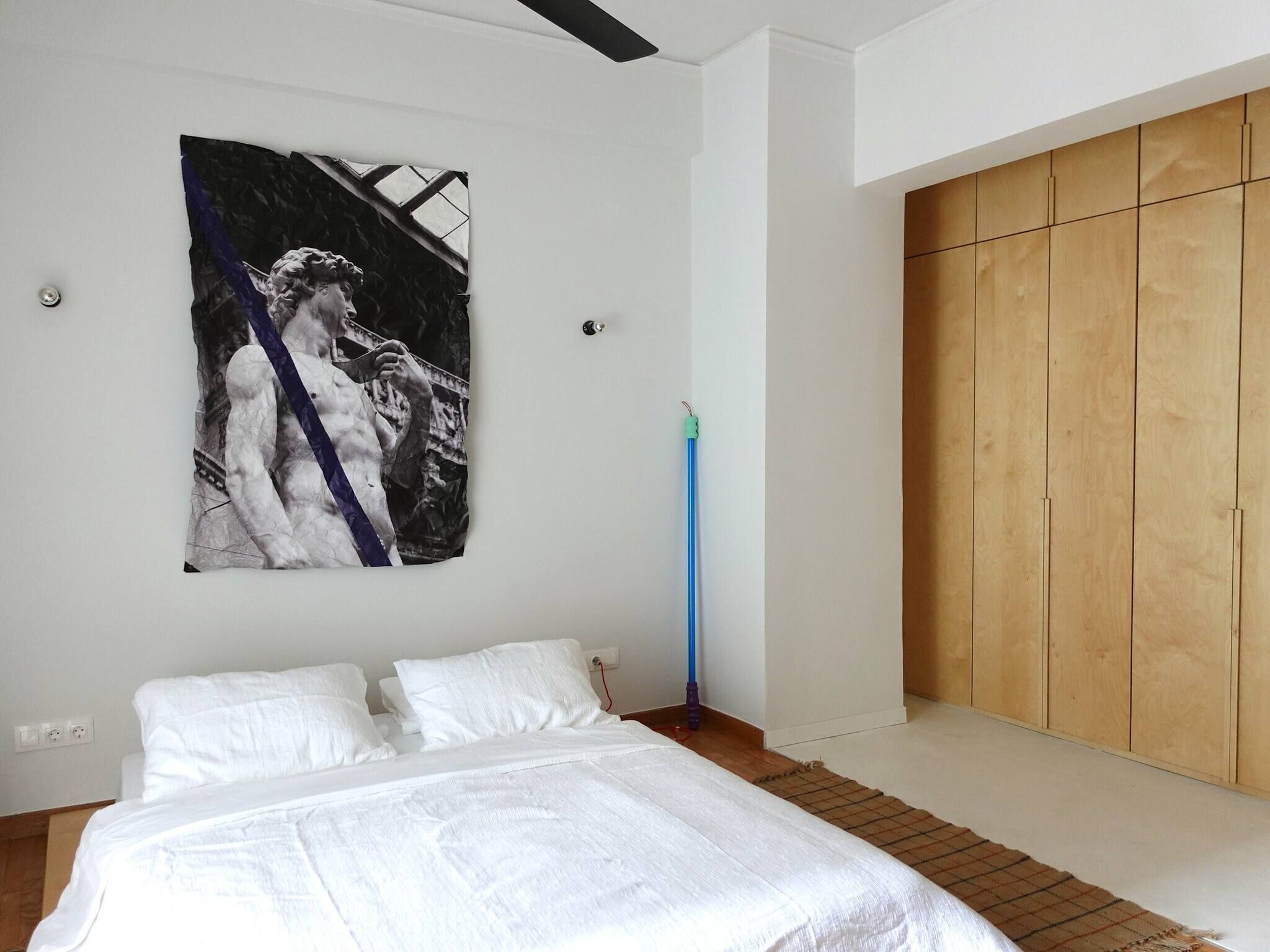 A bedroom with a bed, a wooden wardrobe, and a wall-mounted artwork.