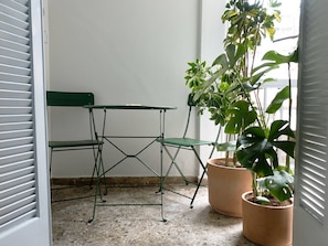 A room with a green metal table and chairs, a potted plant, and a window with blinds.