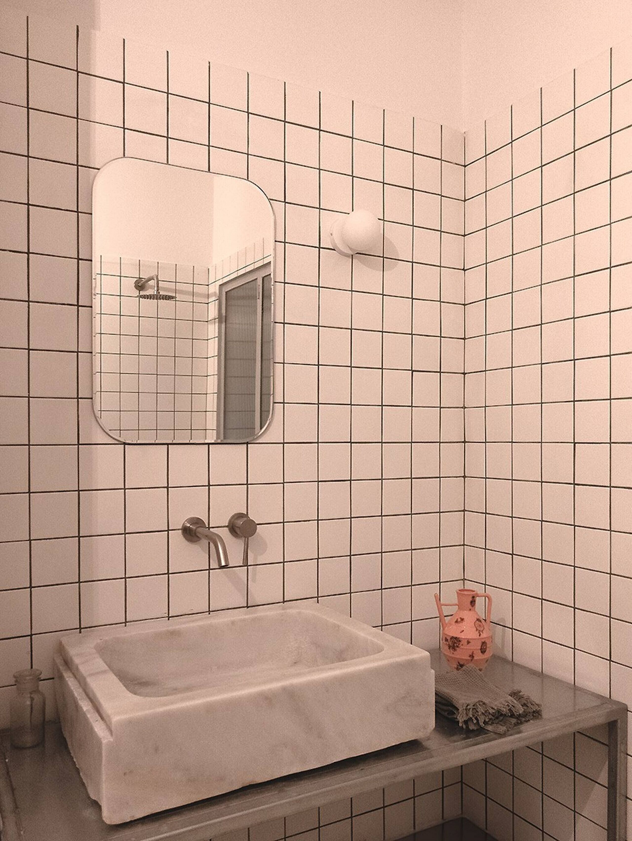 Un bagno con un lavandino rettangolare, uno specchio, una doccetta e un piccolo ripiano con un oggetto decorativo.