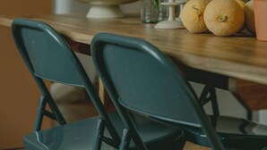 Una mesa de comedor con sillas, un florero con flores, un cuenco y cítricos.