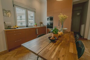 A modern kitchen with a wooden dining table, potted plants, and built-in ovens. - Stylish cozy artistic Athens apartment (Athens)