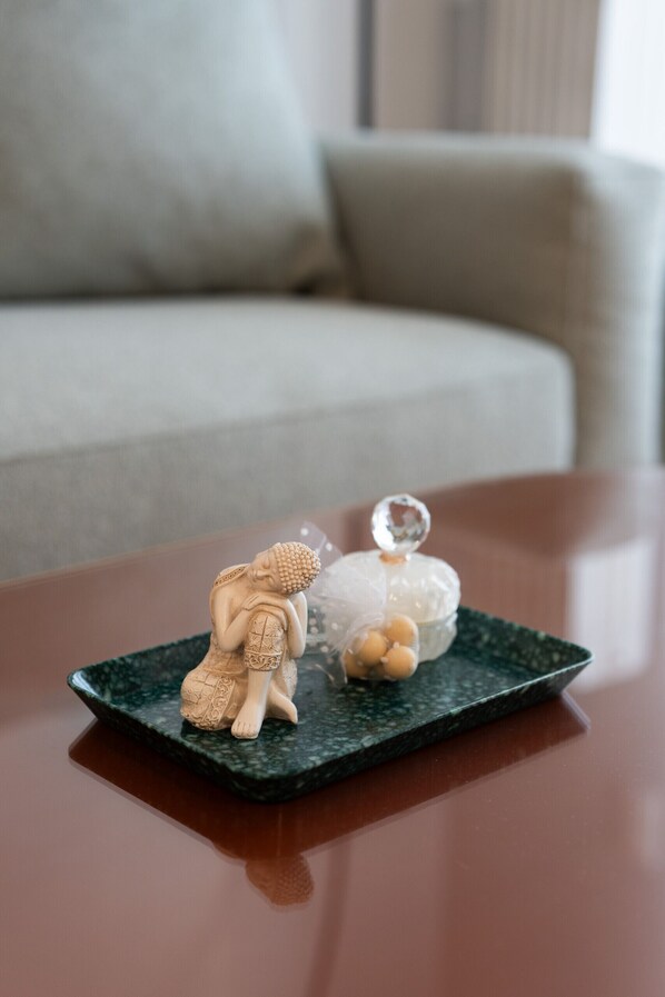 A small Buddha statue on a dark green tray with a crystal on top, placed on a wooden table.