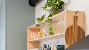 A modern kitchen with a black countertop, a sink, a kettle, and a plant on a shelf.