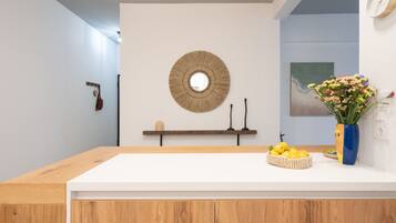 A modern kitchen with a wooden countertop, a round mirror, a shelf with candles, and a vase with flowers.
