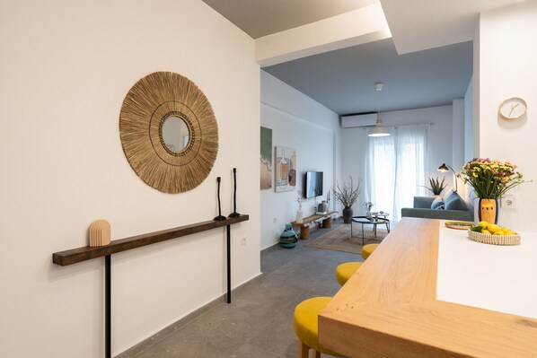 A modern living room with a wooden dining table, yellow chairs, a round mirror, and a sofa. - My Happy Greek Home (Athens)