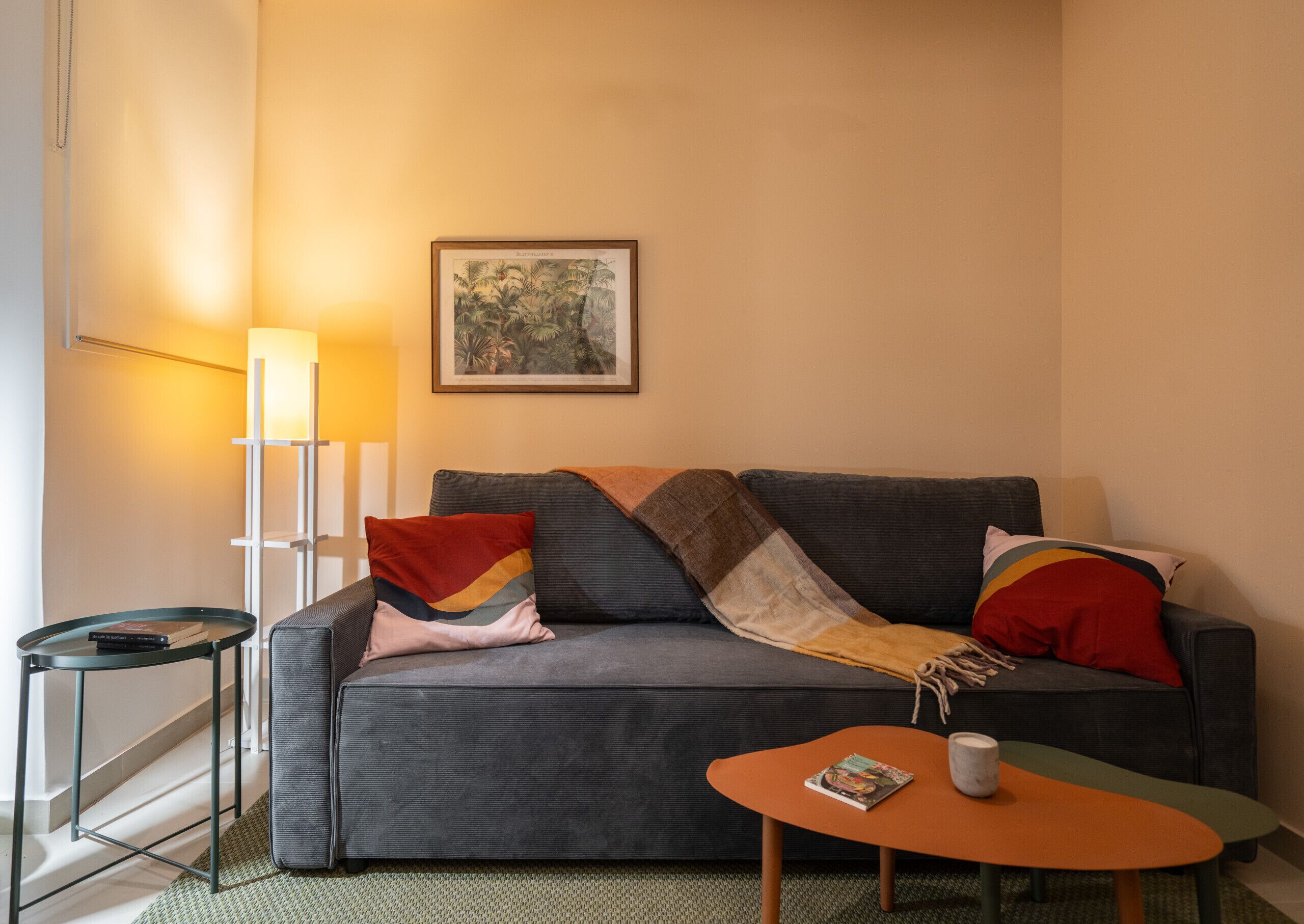 A living room with a sofa, a side table, a lamp, a framed picture, and a small table with a book and a candle.