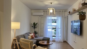 Un salon moderne avec un canapé, un fauteuil à bascule en bois, une lampe et un téléviseur fixé au mur.