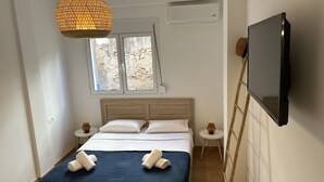 Une chambre d’hôtel moderne dotée d’un grand lit, d’une télévision, d’une fenêtre donnant sur un mur en pierre et d’un appareil de climatisation.