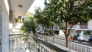 A balcony with a metal railing overlooking a street with parked cars and a tree with orange fruits.