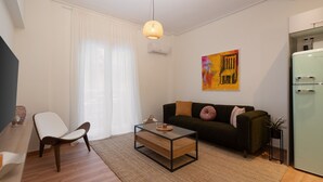 A modern living room with a glass coffee table, a dark green sofa, a white chair, and a small plant.