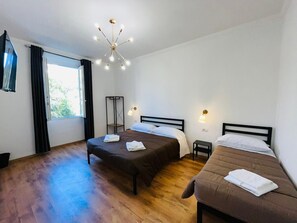 Una camera d'albergo con due letti, una lampada da terra, un lampadario e una finestra con tende.