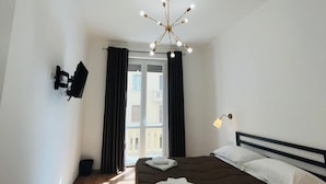 A bedroom with a bed, a TV mounted on the wall, a ceiling light fixture, and a window with curtains. - Prime Rooms Della Loggia (Florence)