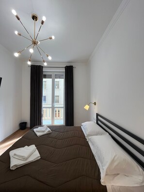 Una moderna camera d'albergo con un grande letto, un lampadario e vista sulla strada attraverso la finestra.