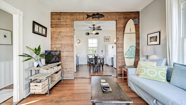 A spacious living area with a wooden floor, a sofa, a coffee table, and a TV on a wooden stand. - The Happy Hut - walk to the beach (Galveston)