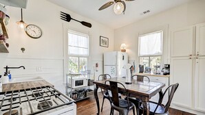 A kitchen with a gas stove, white cabinets, a wooden dining table, and two chairs. - The Happy Hut - walk to the beach (Galveston)
