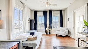 A well-lit room with a bed, a chair, a desk, and a ceiling fan. - The Happy Hut - walk to the beach (Galveston)