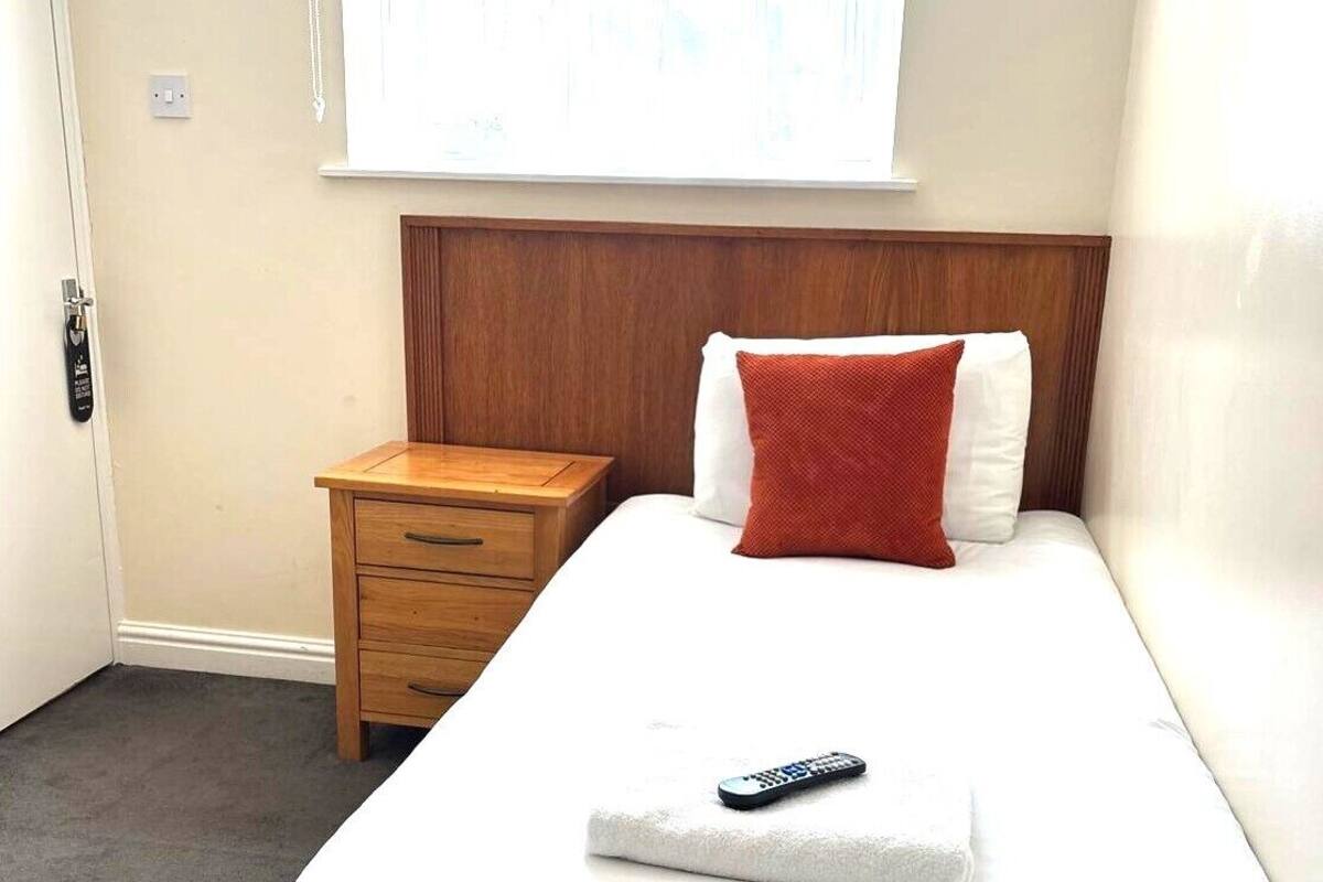 Una habitación de hotel con una cama, una mesita de noche de madera, un control remoto y una ventana con cortinas.