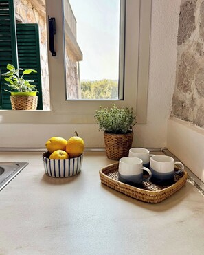 Una encimera de cocina con un bol de limones, una planta en maceta y una bandeja con tazas.