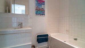 Ein Badezimmer mit einem weißen Waschbecken, einer Badewanne und einer Dusche. An der Wand befindet sich ein Plakat, das ein Schwimmereignis bewirbt.