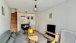 Un salon moderne avec un canapé gris, un fauteuil jaune, un meuble pour la télévision et un coin repas comprenant une table et des chaises.