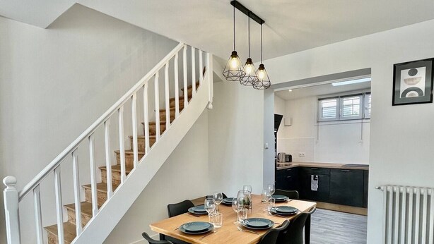 Une cuisine moderne avec une table en bois dressée pour le repas, des chaises noires et un escalier avec des rampes blanches.