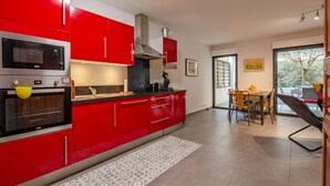 A modern kitchen with red cabinets, a built-in oven, and a dining area with a table and chairs. - Coeur d'Azur - apt climatisé - 1km plage (Saint Raphael)