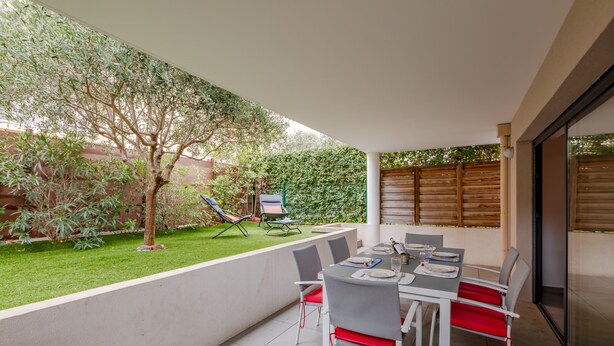 A patio with a table set for dining, surrounded by chairs, and a small garden area with a tree and a lawn. - Coeur d'Azur - apt climatisé - 1km plage (Saint Raphael)