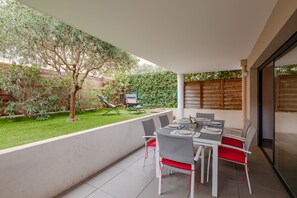 Een terras met een eettafel, omringd door stoelen, en een kleine tuin met een boom en gazon.