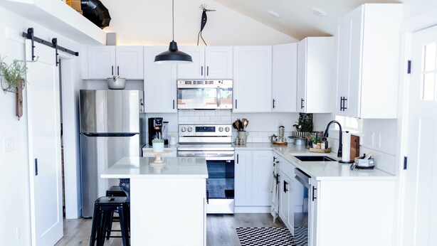 Una cocina moderna con armarios blancos, electrodomésticos de acero inoxidable y una isla central con taburetes.
