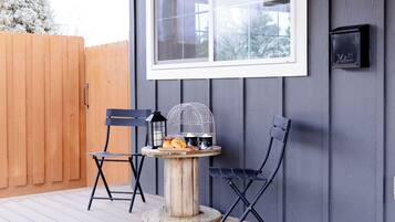 Une terrasse en bois avec deux chaises noires et une petite table ronde agrémentée d’une lanterne et d’une cage à oiseaux.