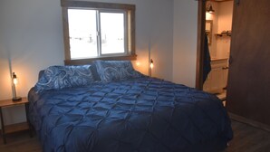 Une chambre avec un grand lit, une fenêtre, une table de chevet et une porte en bois.