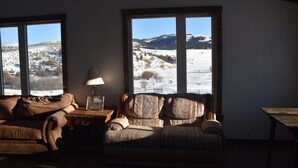 Un salon avec un canapé, une lampe et une vue sur un paysage enneigé, visible à travers de grandes fenêtres.