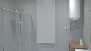 A bathroom with a glass shower enclosure, a white toilet, and a wooden stool.
