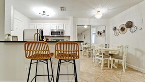 Una cocina moderna con armarios blancos, microondas y un comedor con sillas y mesa blancos.