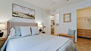 Un dormitorio con una cama grande, una mesita de noche con lámpara, un cuadro en la pared y un banco de madera.