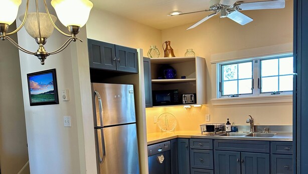 A modern kitchen with a stainless steel refrigerator, a microwave, and a dishwasher. There is a dining table with chairs and a chandelier above.