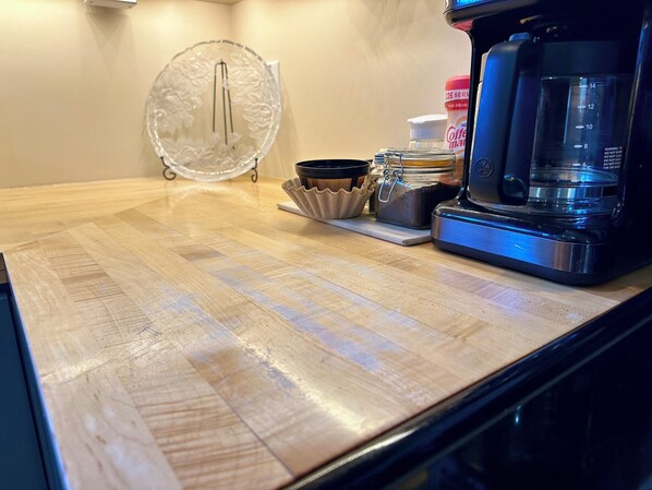 A kitchen counter with a coffee maker, a glass container, and a jar of coffee.