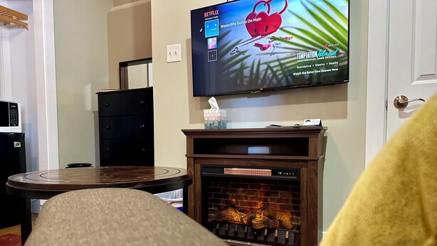 A living room with a fireplace, a television mounted on the wall, and a round table. - King Mountain Suite (Westcliffe)