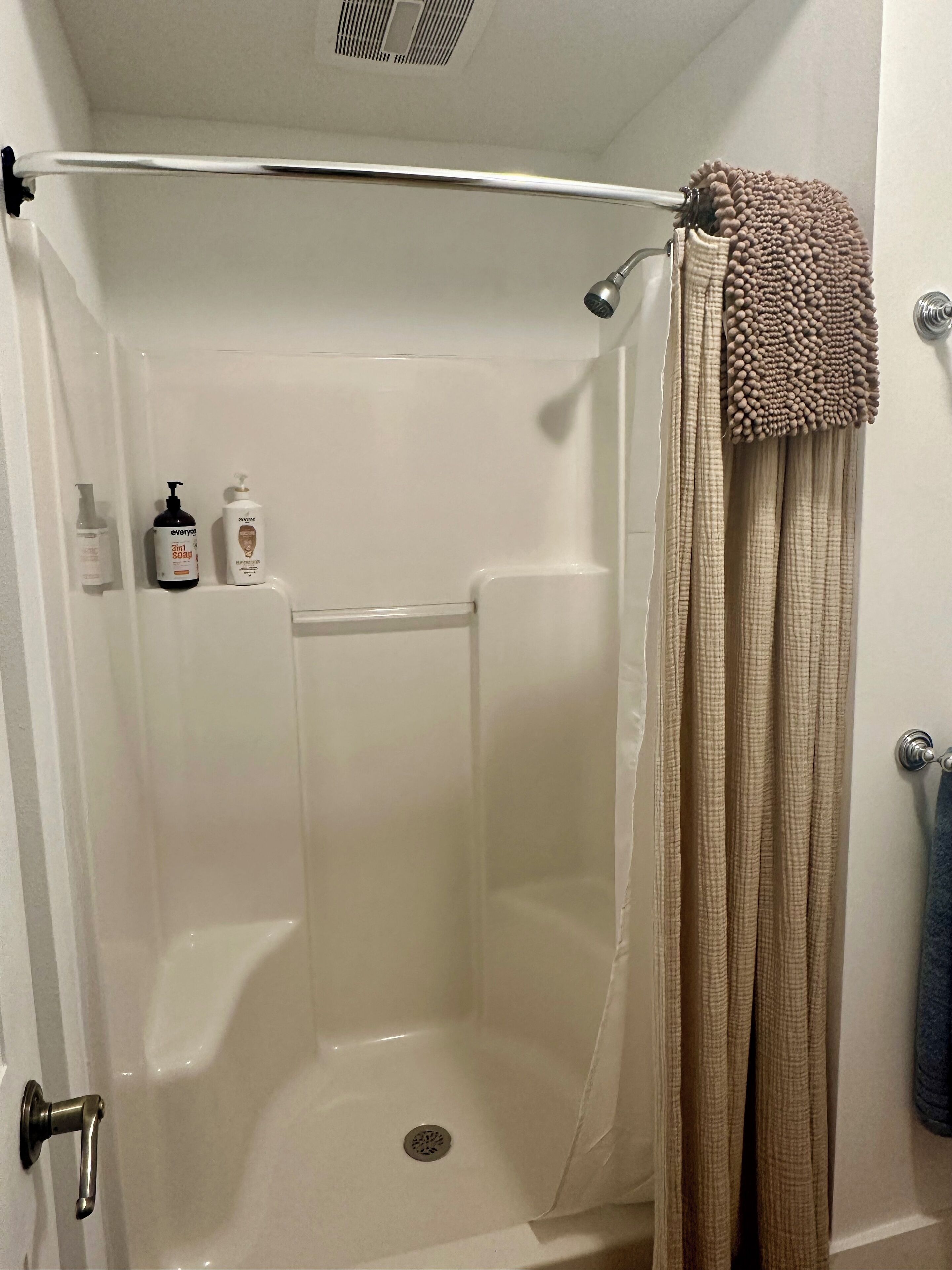Eine Dusche ohne trittfeste Duschwanne mit Glastür, ein Handtuchhalter mit Handtuch und Pflegeprodukten an der Wand.