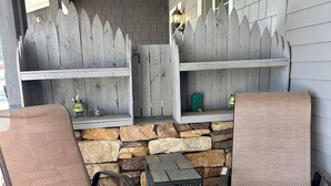 An outdoor patio with two cushioned chairs, a small table, and a stone wall backdrop. - King Mountain Suite (Westcliffe)
