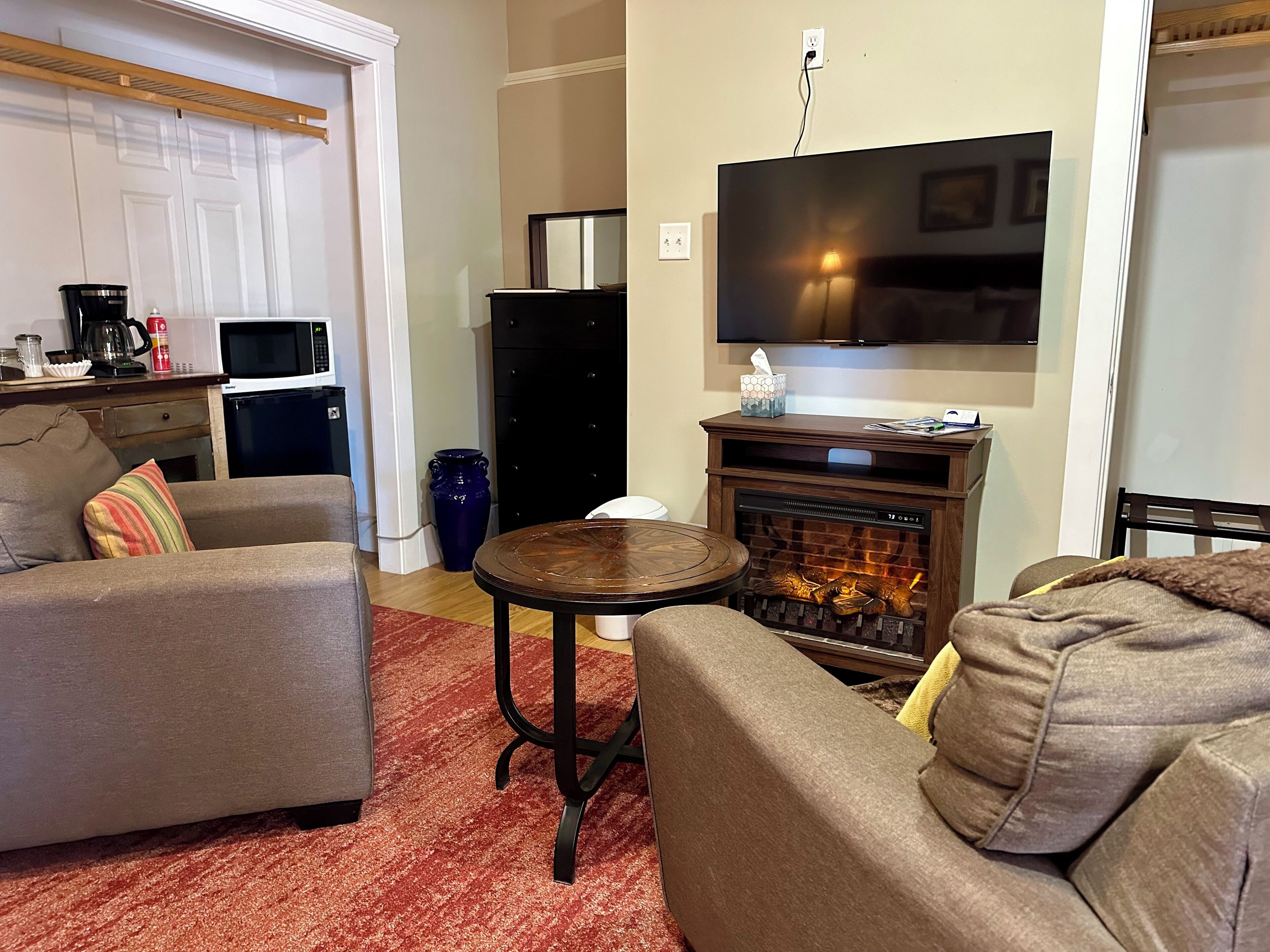 A living room with a fireplace, a television, and a kitchen area in the background.